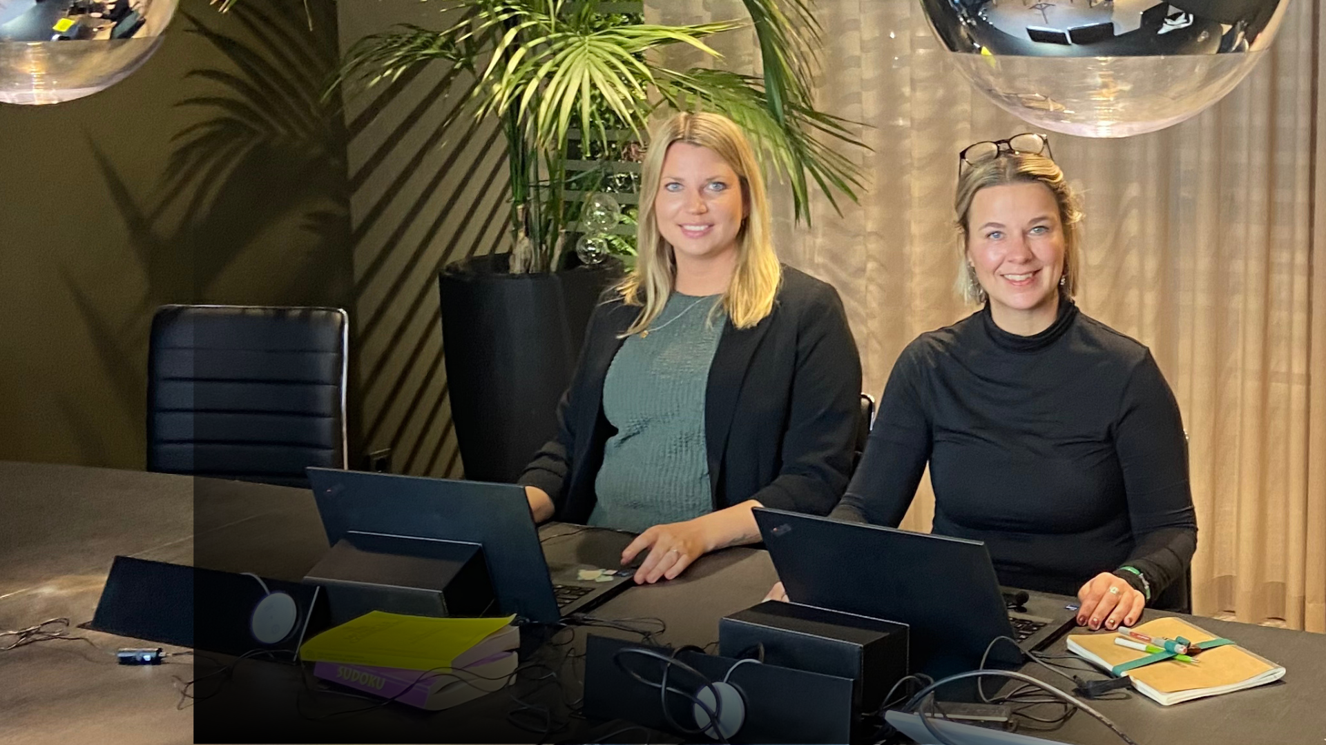 Annica Heuermann och Linda Gårdlöv kollar in i kameran och sitter runt ett bord